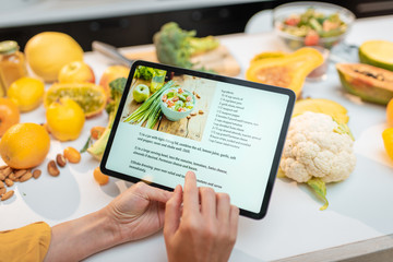 Woman looking on the digital recipe, using touchscreen tablet while cooking healthy meal on the...