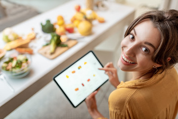 Portrait of a happy woman shopping food online using a digital tablet at the kitchen, close-up view...