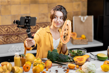 Young and cheerful woman vlogging on mobile phone about healthy food and cooking. Concept of healthy eating and social media influencing