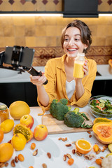Young and cheerful woman vlogging on mobile phone about healthy food and cooking. Concept of healthy eating and social media influencing