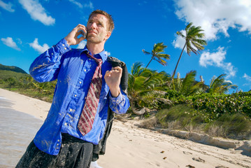 Businessman standing on a tropical island beach in a sea-soaked suit trying to get a signal on his...