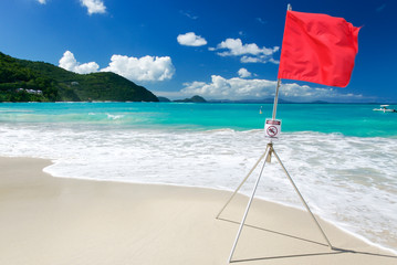 Bright sunny view of red flag standing in the waves of a tropical island beach