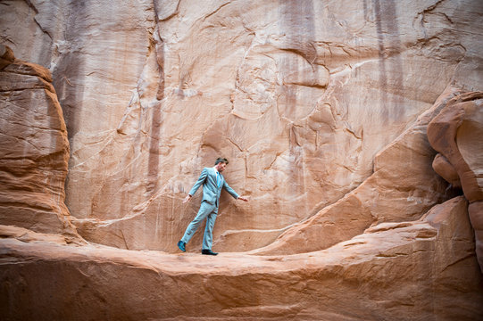 Nervous businessman taking a tentative step on a narrow ledge in a red rock canyon