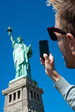 Personal pov perspective of tourist taking picture of the Statue of Liberty with his smartphone