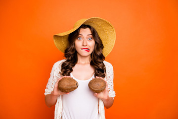 Photo of funny uncertain curly wavy girlfriend holding two coconuts near her tits biting her lips...