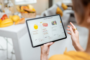 Woman shopping food online using a digital tablet at the kitchen, close-up view on a tablet screen....