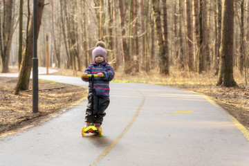 a child races on a scooter along an asphalt road in a spring park