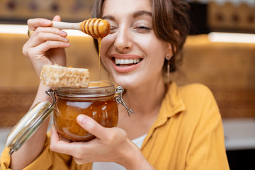 Portrait of a young and cheerful woman with a jar full of sweet honey on the kitchen at home