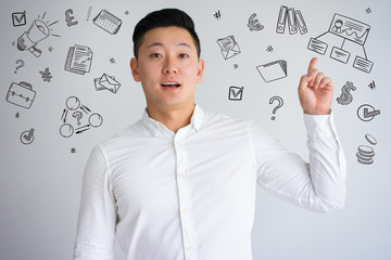 Asian guy pointing finger up with hand drawn business sketches. Excited man raising hand. Young...