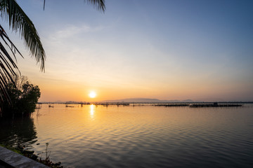 Sunrise view from lake with beautiful twilight sky, smooth water surface, mountain in background and coconut tree infront.