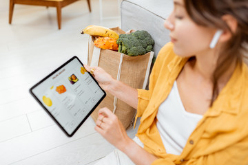 Young woman shopping online using a digital tablet, sitting with bag full of products at home. Concept of buying online using mobile devices