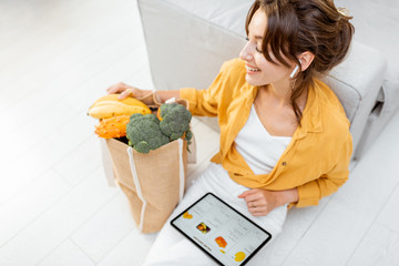 Young woman shopping online using a digital tablet, sitting with bag full of products at home....