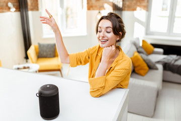 Happy young woman controlling smart home devices with a voice commands and smart speaker at home....