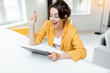 Young and cheerful woman using a digital tablet while sitting relaxed at home. Concept of a leisure...