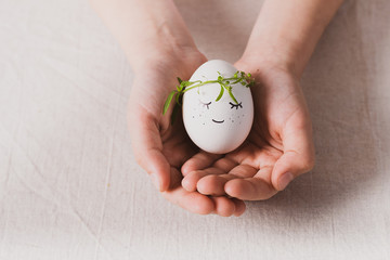 Festive composition Easter egg with a funny muzzle with eyes in the hands child. Happy easter concept. Horizontal frame