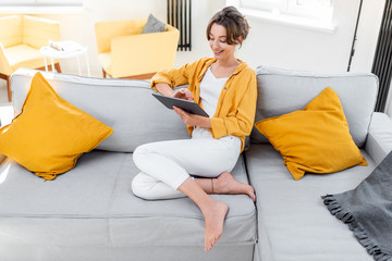 Young and cheerful woman using a digital tablet while sitting relaxed on the couch at home. Concept of a leisure activities with mobile devices at home © rh2010