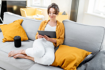 Young and cheerful woman using a digital tablet while sitting relaxed on the couch at home. Concept...