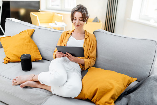 Young and cheerful woman using a digital tablet while sitting relaxed on the couch at home. Concept of a leisure activities with mobile devices at home