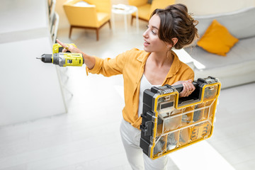 Portrait of a young and beautiful handy woman standing with a screwdriver and instrument box at the...