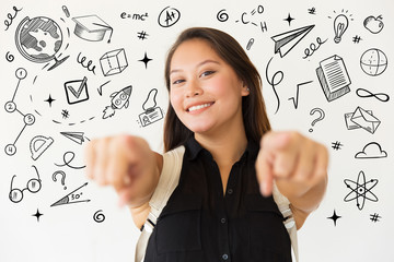 Happy young woman pointing at camera. Cheerful female student with backpack pointing with fingers with hand drawn studying sketches around her. Education concept