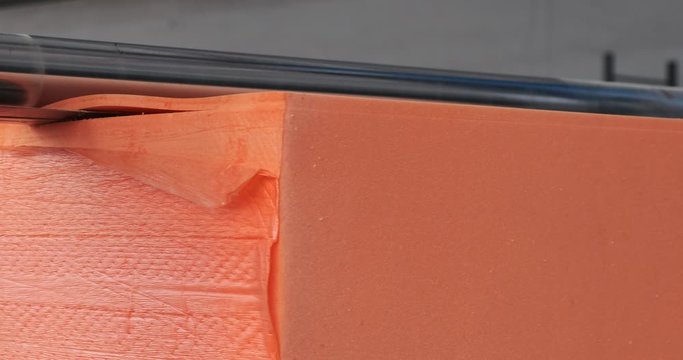 Factory machine cuts foam sponge blanks for kitchen sponges. With huge knife, he cuts the orange foam, creating desired shape for the future product. Automated production without human intervention