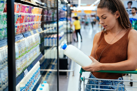 Female buying milk in supermarket stock photo. Young woman checking milk's labeling in supermarket