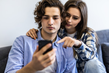 Cute young couple relaxing on couch with smartphone at home in the living room