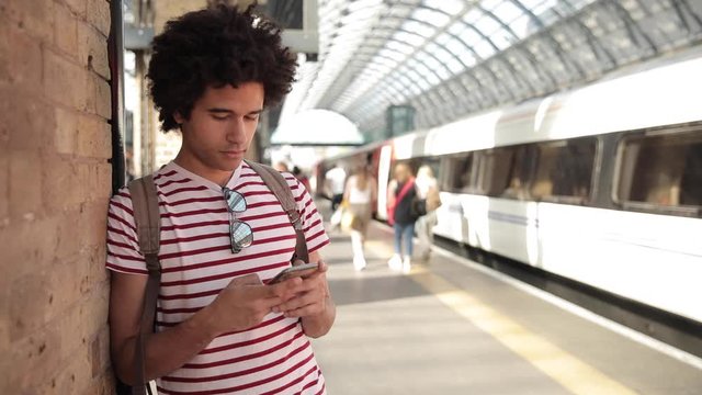 Man at train station checking timetables on mobile phone