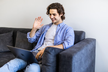 Young relaxed man video-calling on Internet sitting on couch at home