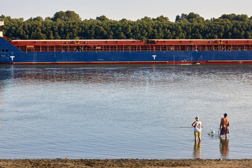 Fishermen on the river bank and cargo ship