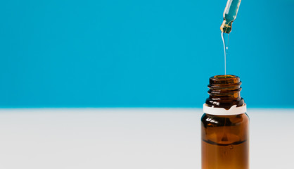 cosmetics, hyaluronic acid flows from a pipette into a glass bottle on a blue background