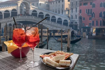 Küchenrückwand glas motiv Cocktail, Aperitif für zwei mit Blick auf Venedig im Hintergrund. Zwei Gläser Spritz mit Zitrone und Strohhalmen und ein Teller mit Snacks © cesaresent