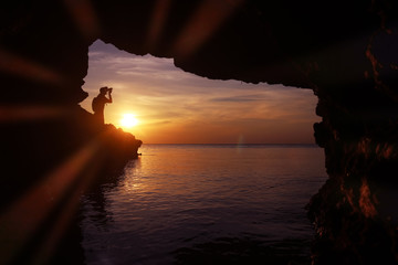 Silhouette of photographer using the camera to take photo of the sunset in a cave by the sea