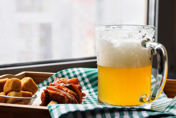 mug of light fresh beer with foam, pieces of fish on a towel near the window, alcoholic drink