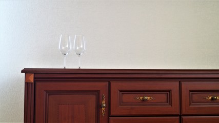 two wine glasses on a wooden chest of drawers on a white wall background