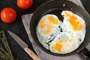 fried eggs in a frying pan , tomatoes, towel, knife, thyme, shell on a black