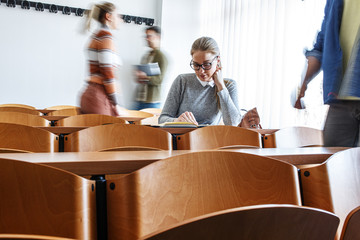  In the university classroom, a beautiful female student joins her peers, books and notes in hand,...