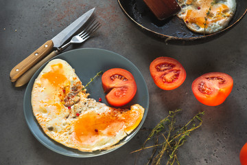 scrambled eggs with tomato on a plate , knife and fork on a gray