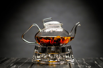 Horizontal photo of the tea set on a black background. Glass transparent teapot and cup. Black leaf...