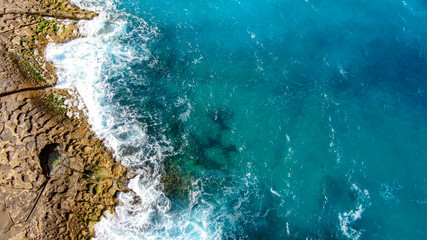 Wonderful turqouise blue ocean water hitting against the rocks - top down view - aerial photography