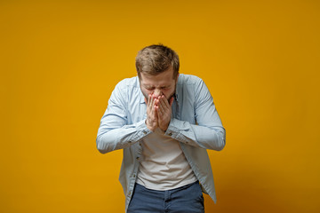 Caucasian man coughs or sneezes while covering mouth with palms. Concept of the spread of the virus.