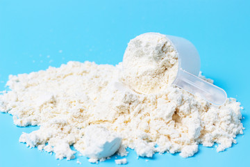 Scattered protein and measuring spoon on blue background, concert of sports nutrition.