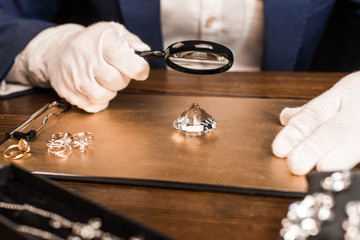 Cropped view of jewelry appraiser examining gemstone with magnifying glass near jewelry on board on table isolated on black