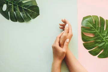 Photo sur Plexiglas ManIcure Manucure pastel sur fond bleu et rose avec des feuilles de palmier. Fond tropical avec les mains de la femme