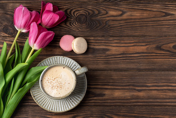 Obraz na płótnie Canvas pink tulips, cup with coffee and macaroons on a wooden background, copy space