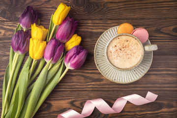 Obraz na płótnie Canvas purple and yellow tulips, cup with coffee and macaroon cookies, pink satin ribbon on a wooden background, copy space