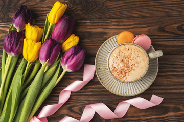 purple and yellow tulips, cup with coffee and macaroon cookies, pink satin ribbon on a wooden background, copy space