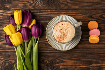purple and yellow tulips, cup with coffee and macaroon cookies on a wooden background, copy space