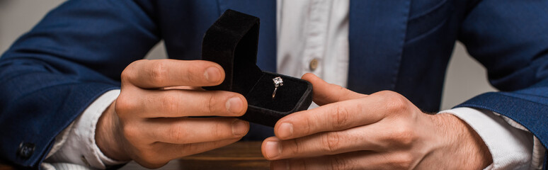 Cropped view of jewelry appraiser holding box with jewelry ring at table isolated on grey, panoramic shot