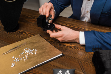 Cropped view of jewelry appraiser examining jewelry ring with magnifying glass near gemstones on...